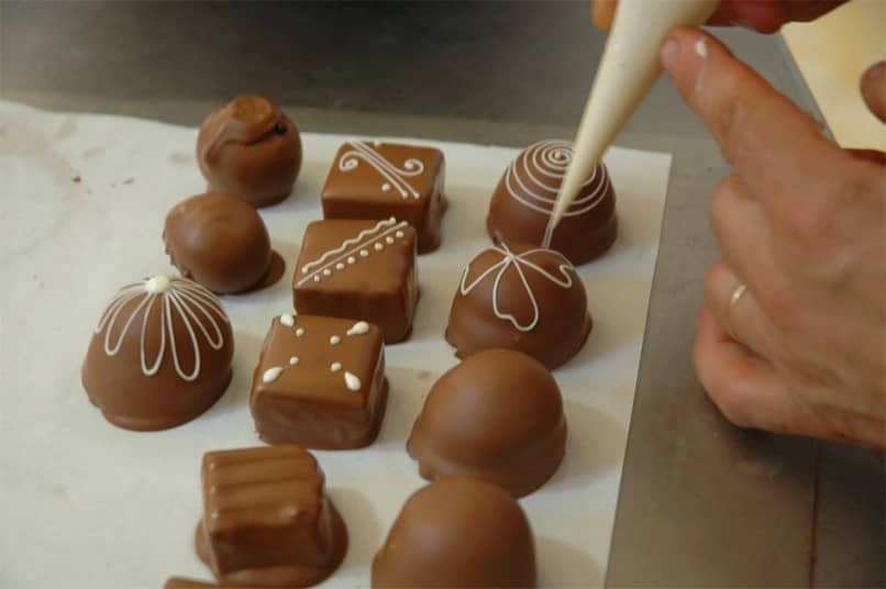 persona a mano decorando pequenos chocolates
